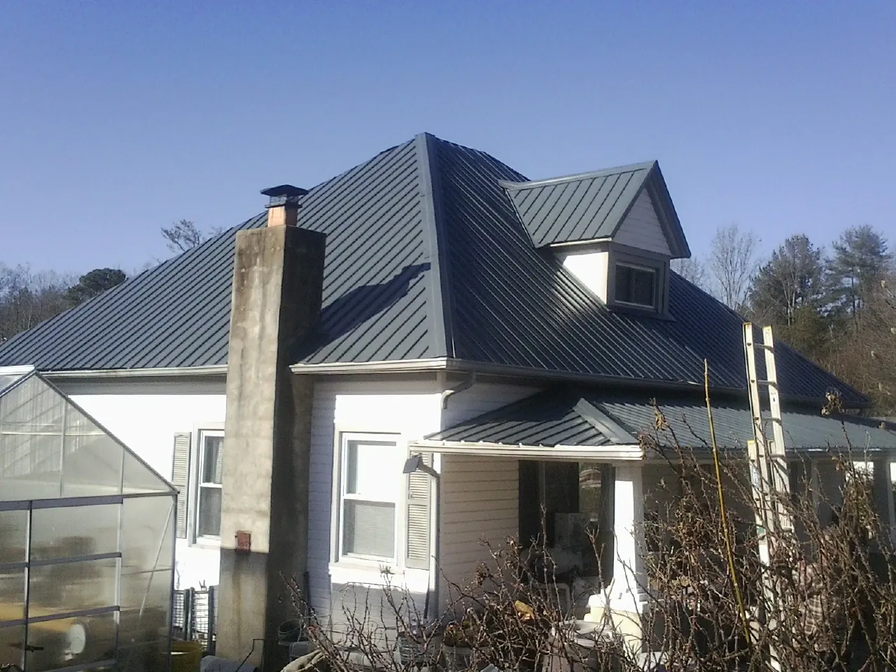 Dark blue standing seam metal roof on a white farmhouse with dormer in Spring Glen