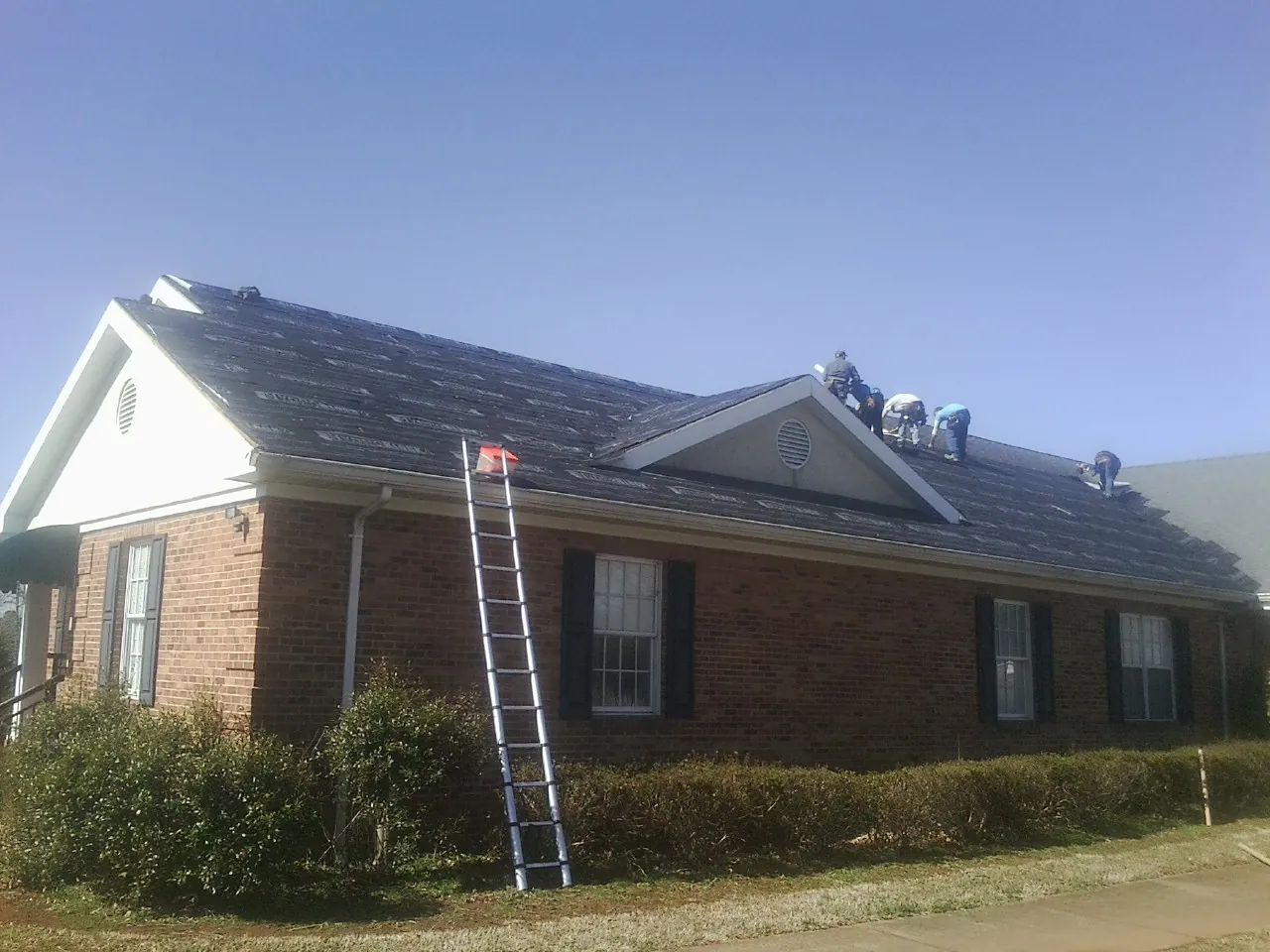 Crew tearing shingles off a brick ranch roof with a ladder set — Metal Roof Repair work by our crew in Spring Glen