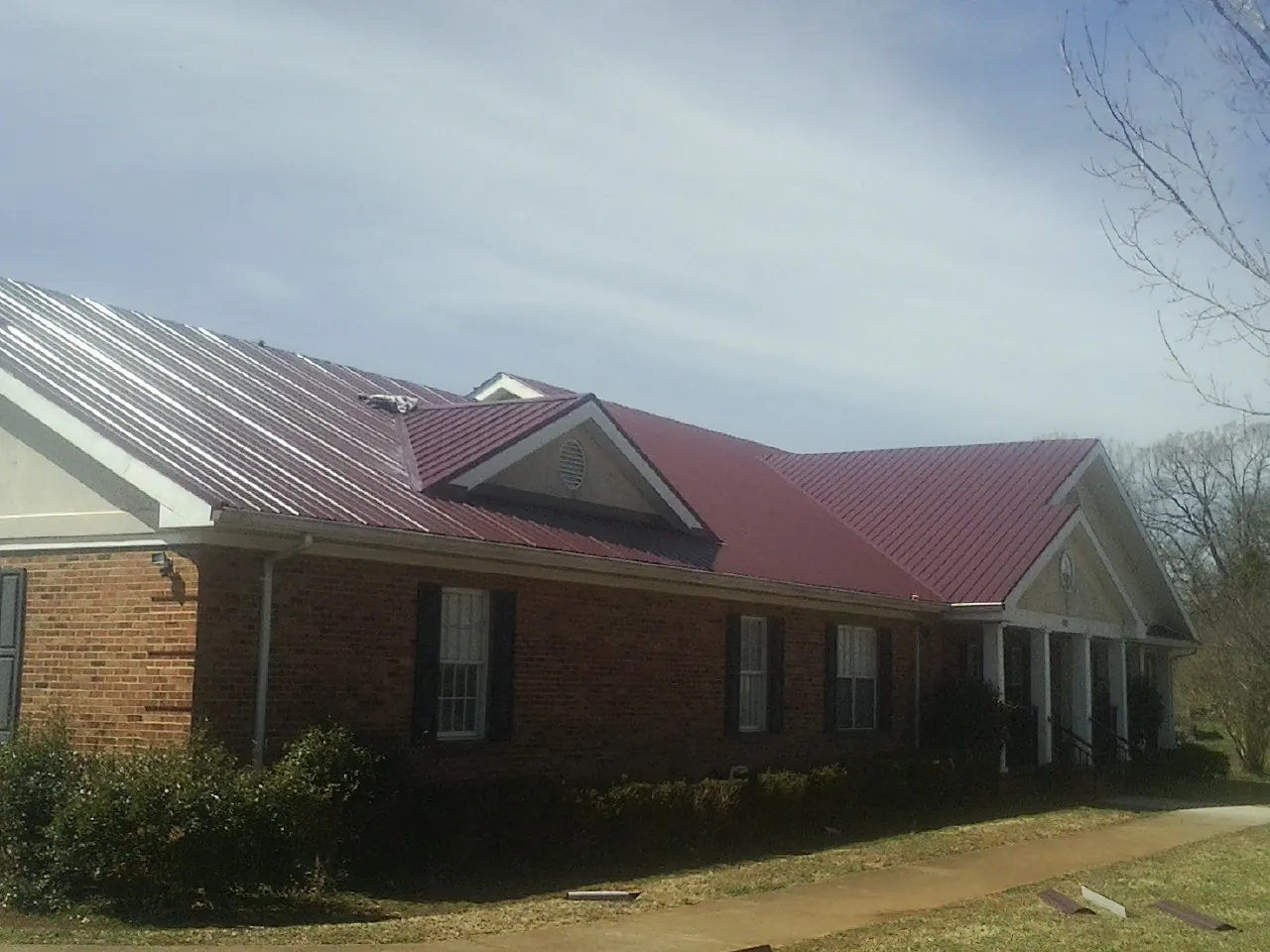 Red metal roof with gabled entries on a long brick building, from a Hail Damage Roof Repair job in Spring Glen
