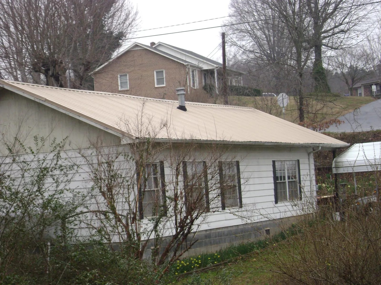 Tan metal roof on a white sided house set into a hillside — Commercial Roofing by Roofing Brothers in Spring Glen
